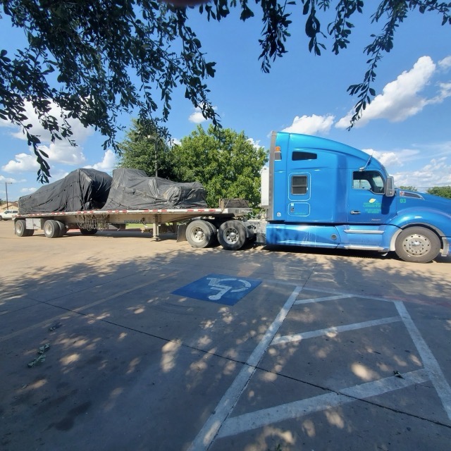 Blue Kenworth tractor hooked to a flatbed carrying tarped industrial machinery for heavy haul transport