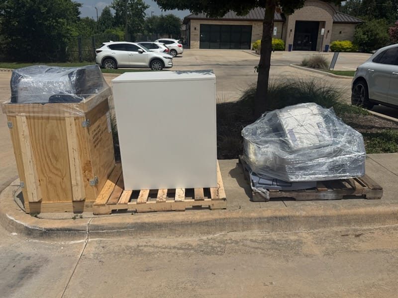 Crated and shrink-wrapped electrical equipment staged on pallets at a curbside white-glove delivery