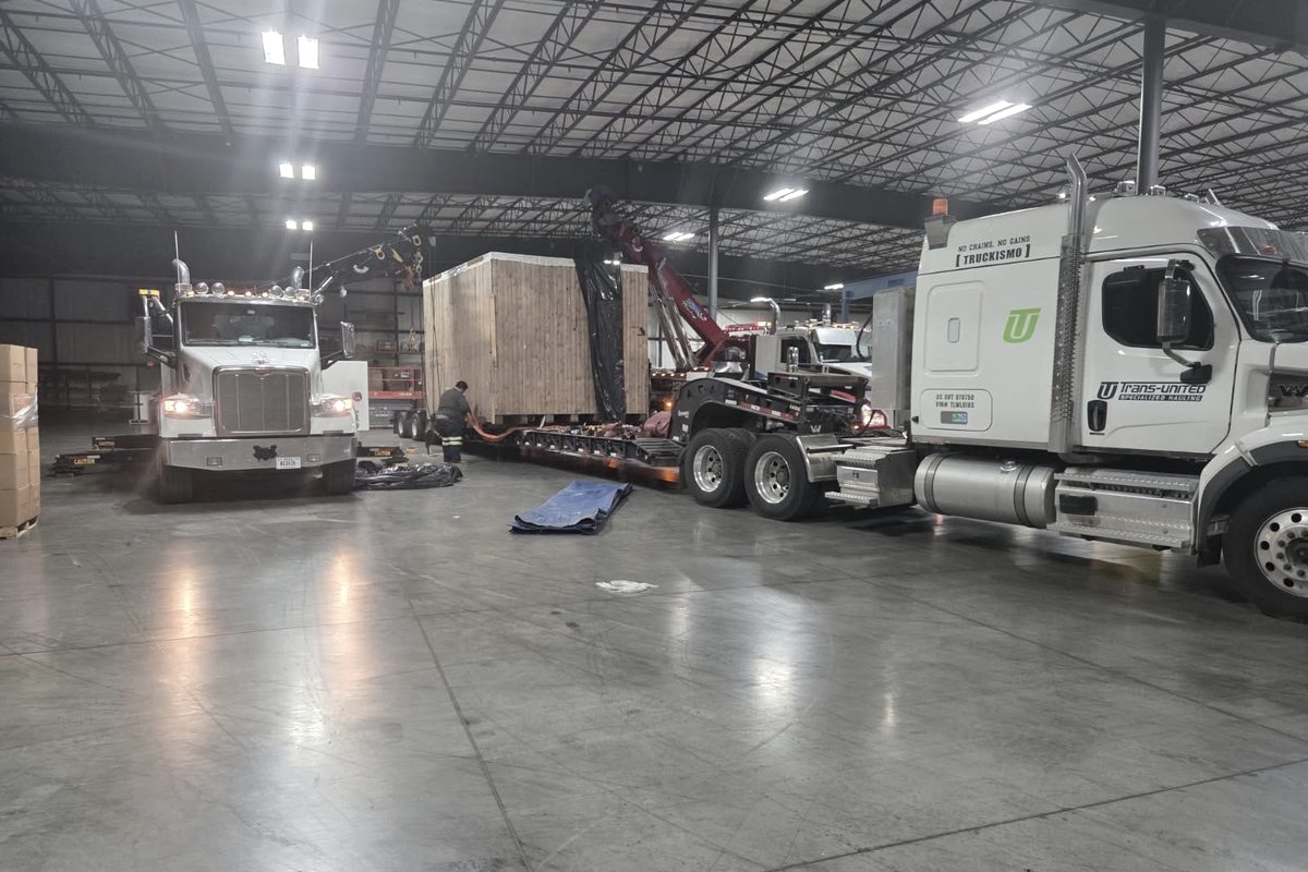 Electric warehouse forklift staged at a loading dock for transport on a flatbed trailer